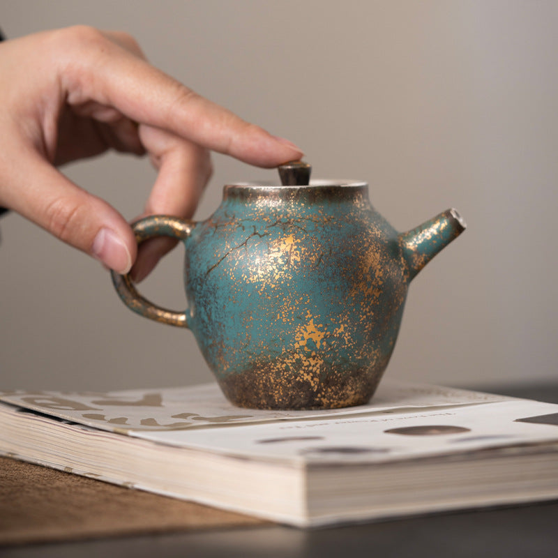 Golden-Azur Aureated Kiln Trans Compact Teapot with one hand pinching the lid button