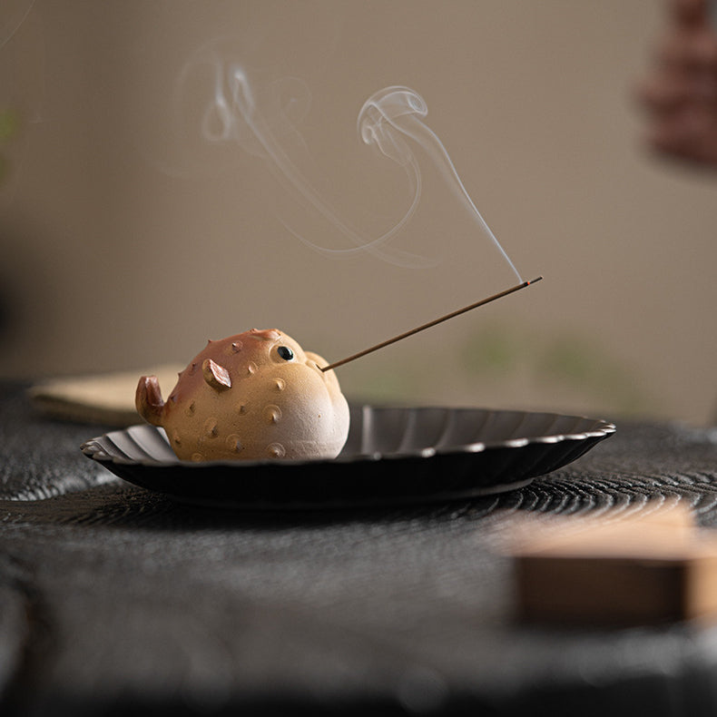 Close up shot of the Purple-Sand Mud Puffer Fish Incense Holder holding a burning stick incense